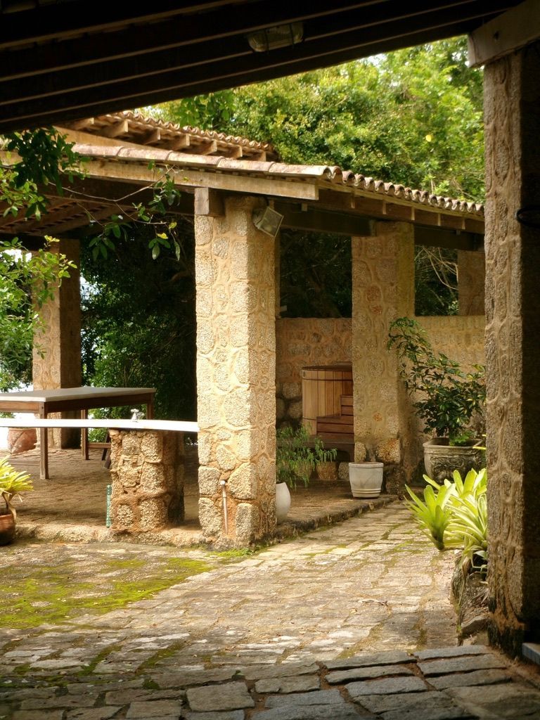 Pátio de pedra com pérgola, colunas e vasos de plantas em um pátio ajardinado sombreado.