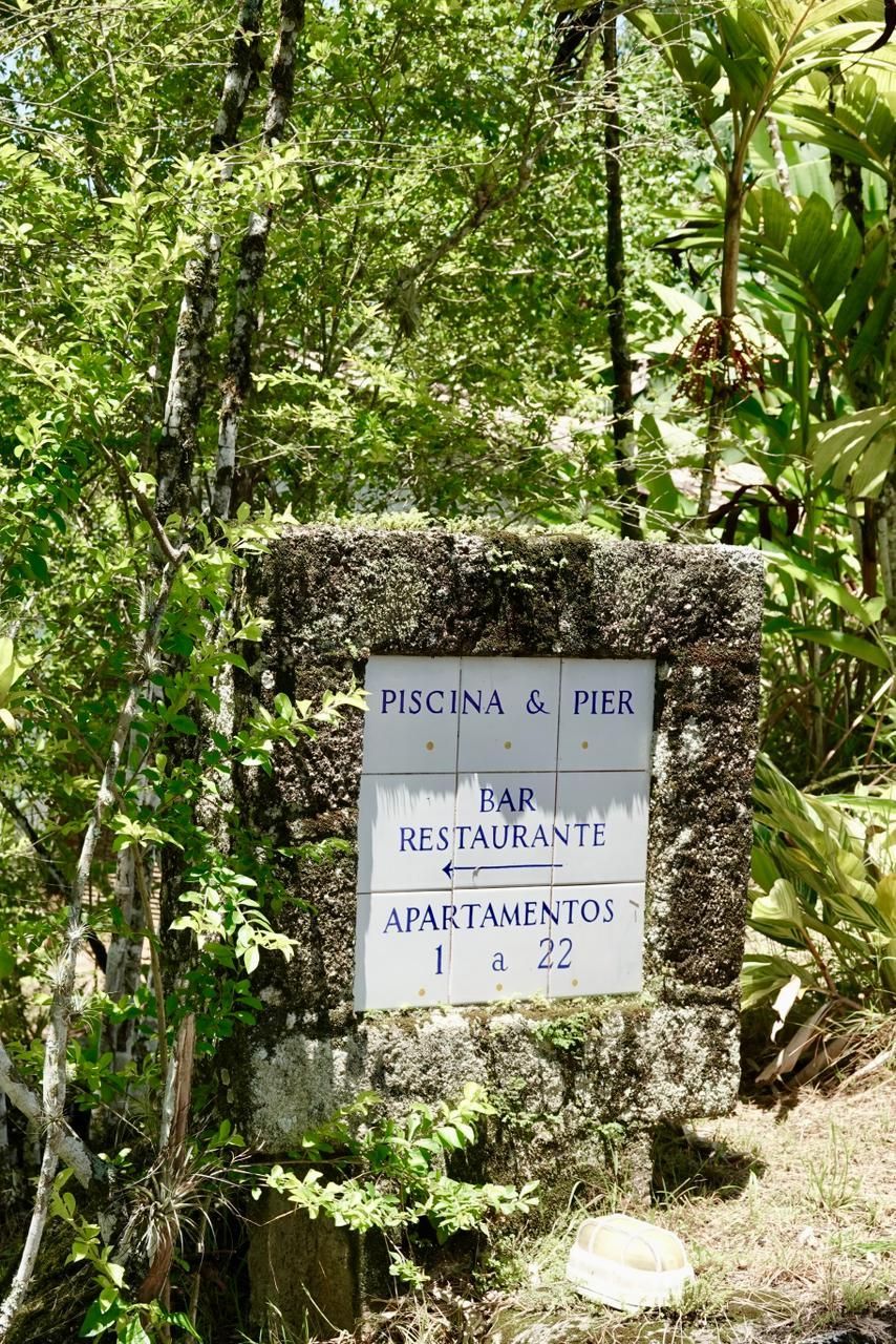 Placa de pedra na entrada da floresta com a inscrição “Piscina a Pie” e o endereço.