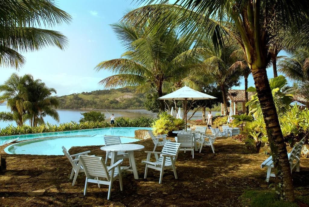 Resort tropical à beira da piscina com espreguiçadeiras brancas, guarda-sóis, palmeiras e água turquesa perto da praia.