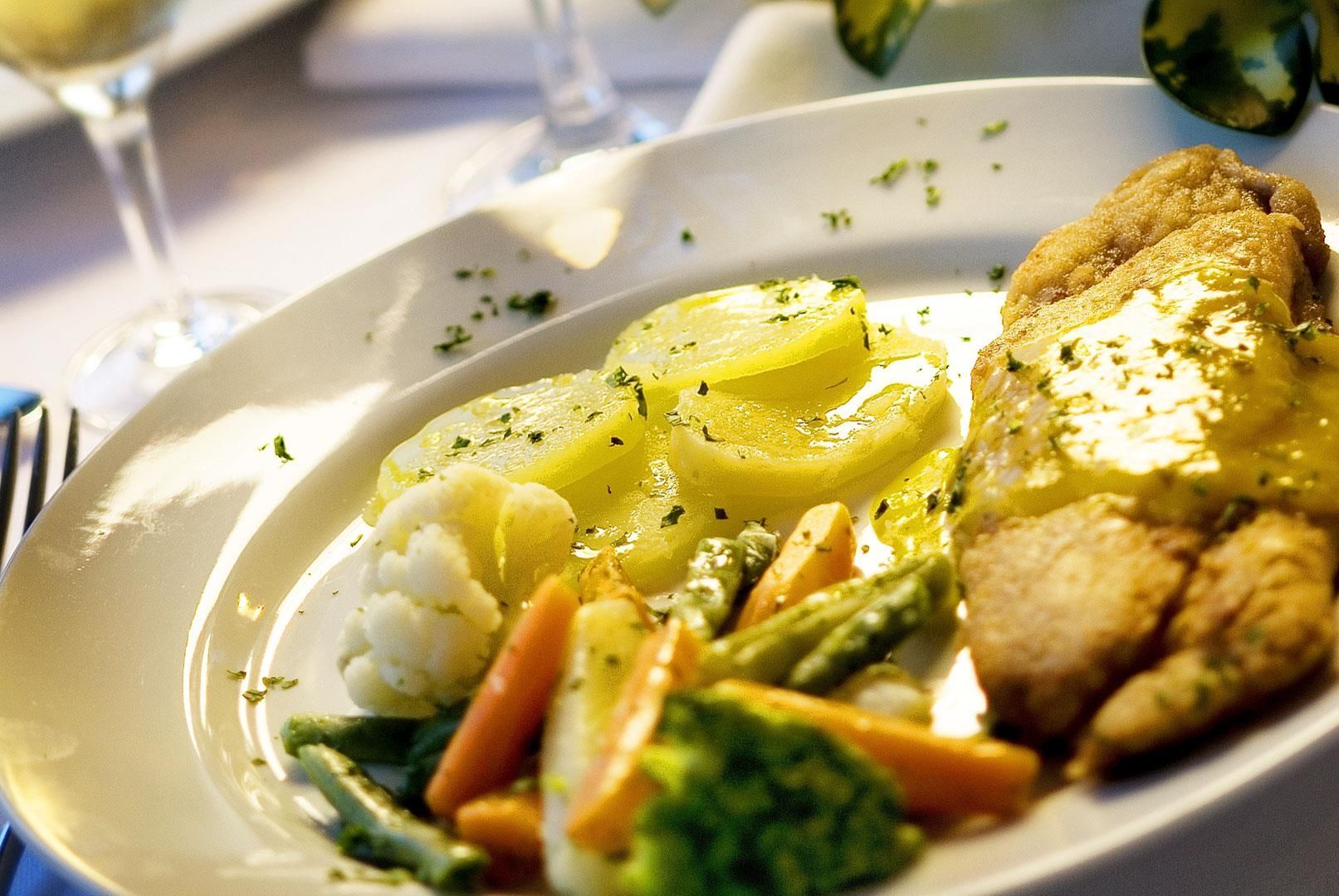 Prato branco com frango, legumes e purê de batatas sobre uma mesa de jantar.