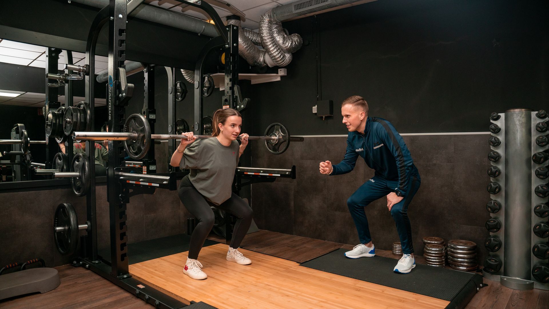 een man en een vrouw hurken met een halter in een sportschool.