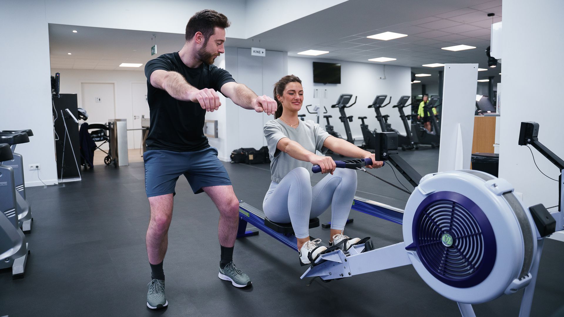 Een man helpt een vrouw met oefenen op een roeimachine in een sportschool.