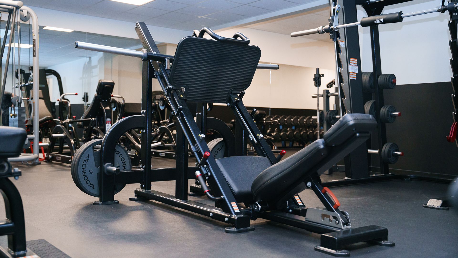 Een sportschool vol met veel fitnessapparatuur, waaronder een legpressmachine.