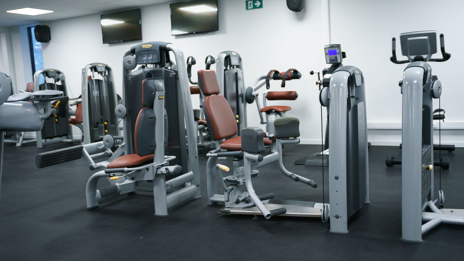 Een sportschool met veel fitnessapparatuur op de vloer.