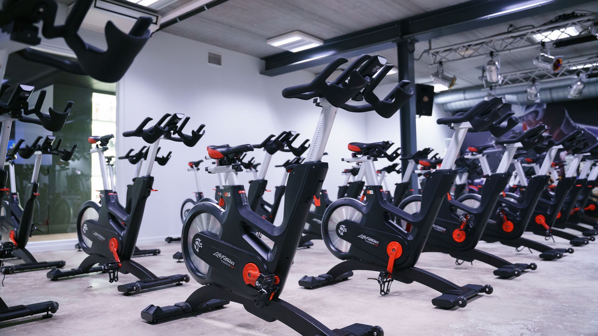 In een sportschool staat een rij hometrainers opgesteld.