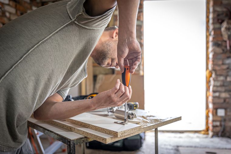 Person using a screwdriver to assemble a wooden board in a home renovation setting
