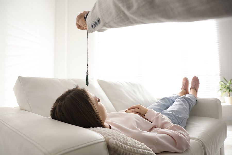 Woman on couch being hypnotized with a pendulum in a brightly lit room.