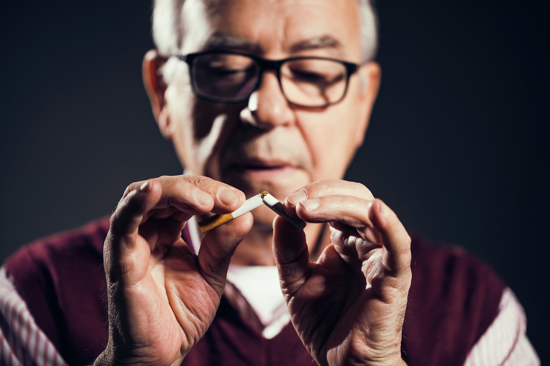 Older man with glasses breaking a cigarette, quitting smoking.