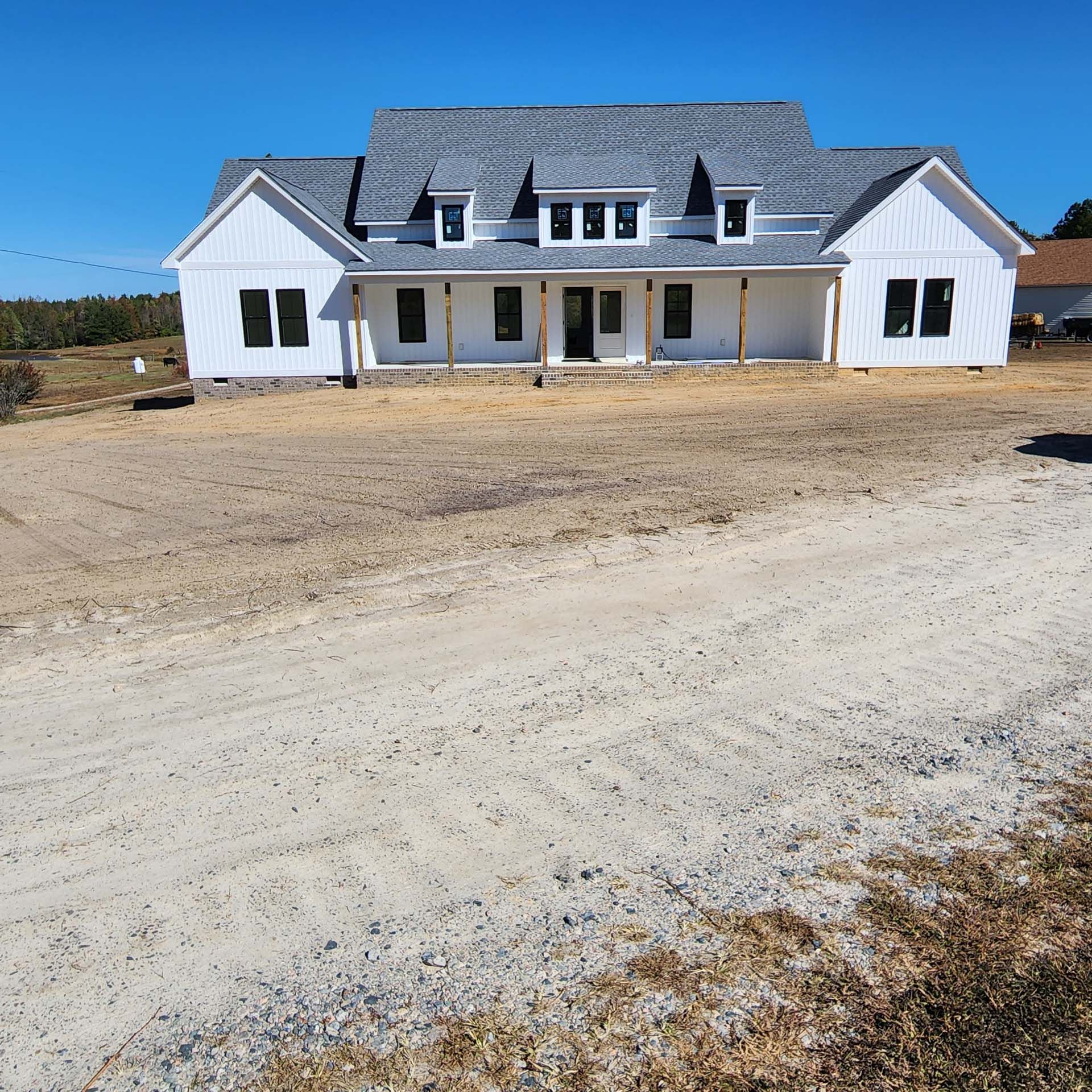 A white house with a gray roof is sitting on a dirt road