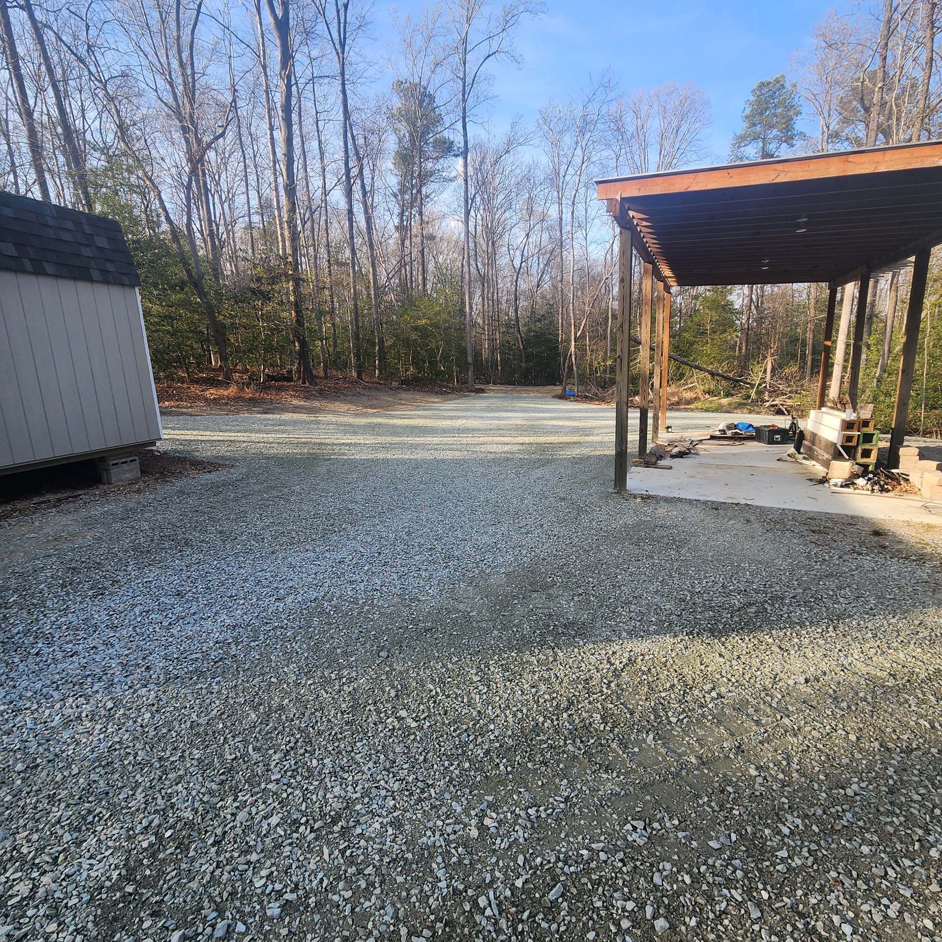 A gravel driveway with a shed in the background and trees in the background.