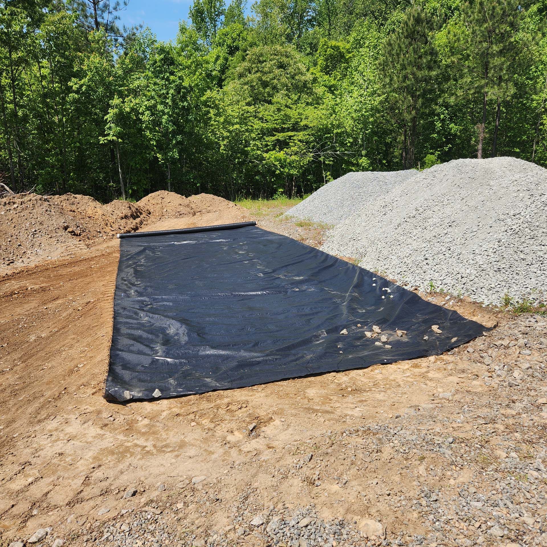 A large black tarp is laying on the ground next to a pile of gravel.
