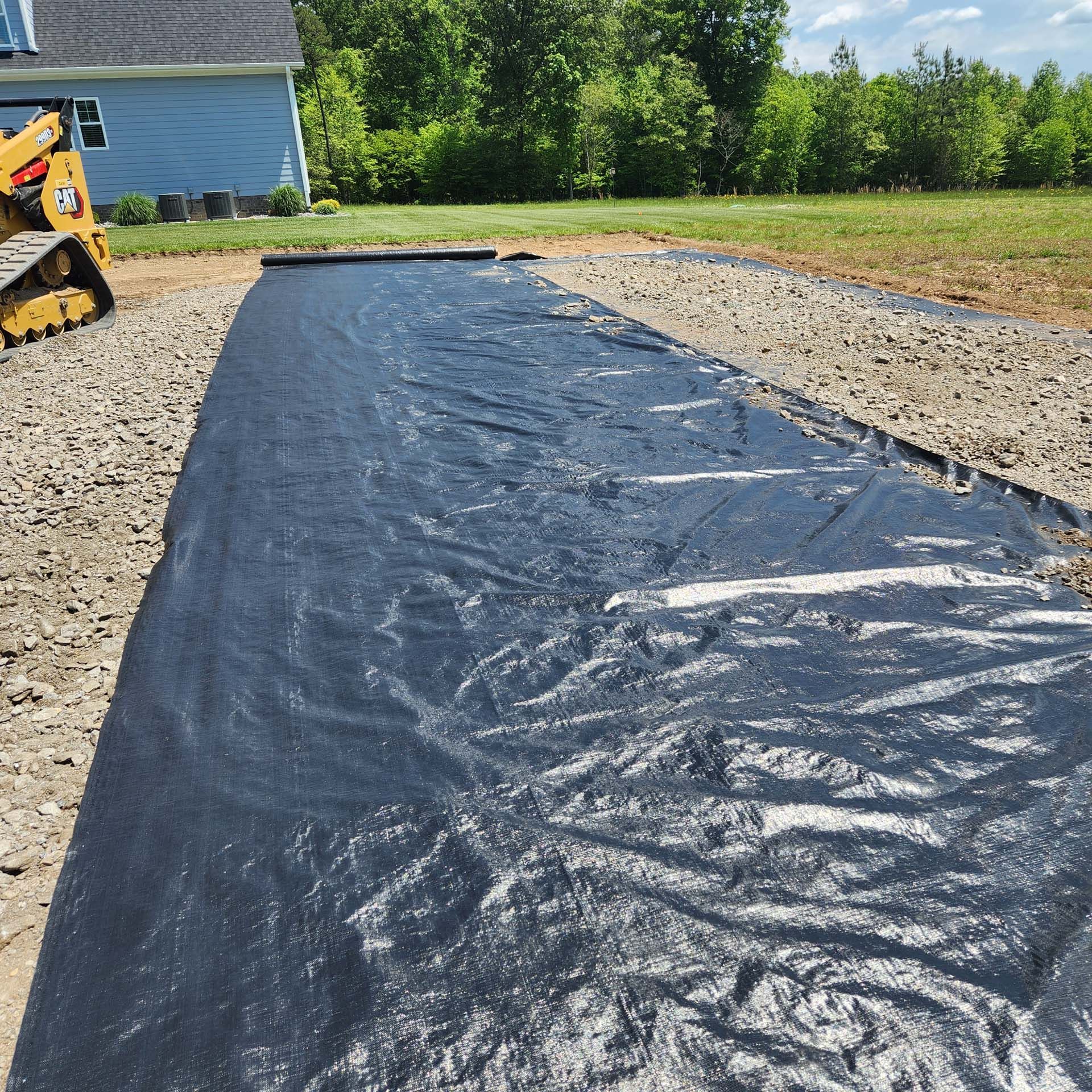 A black tarp is covering a dirt road in front of a house.
