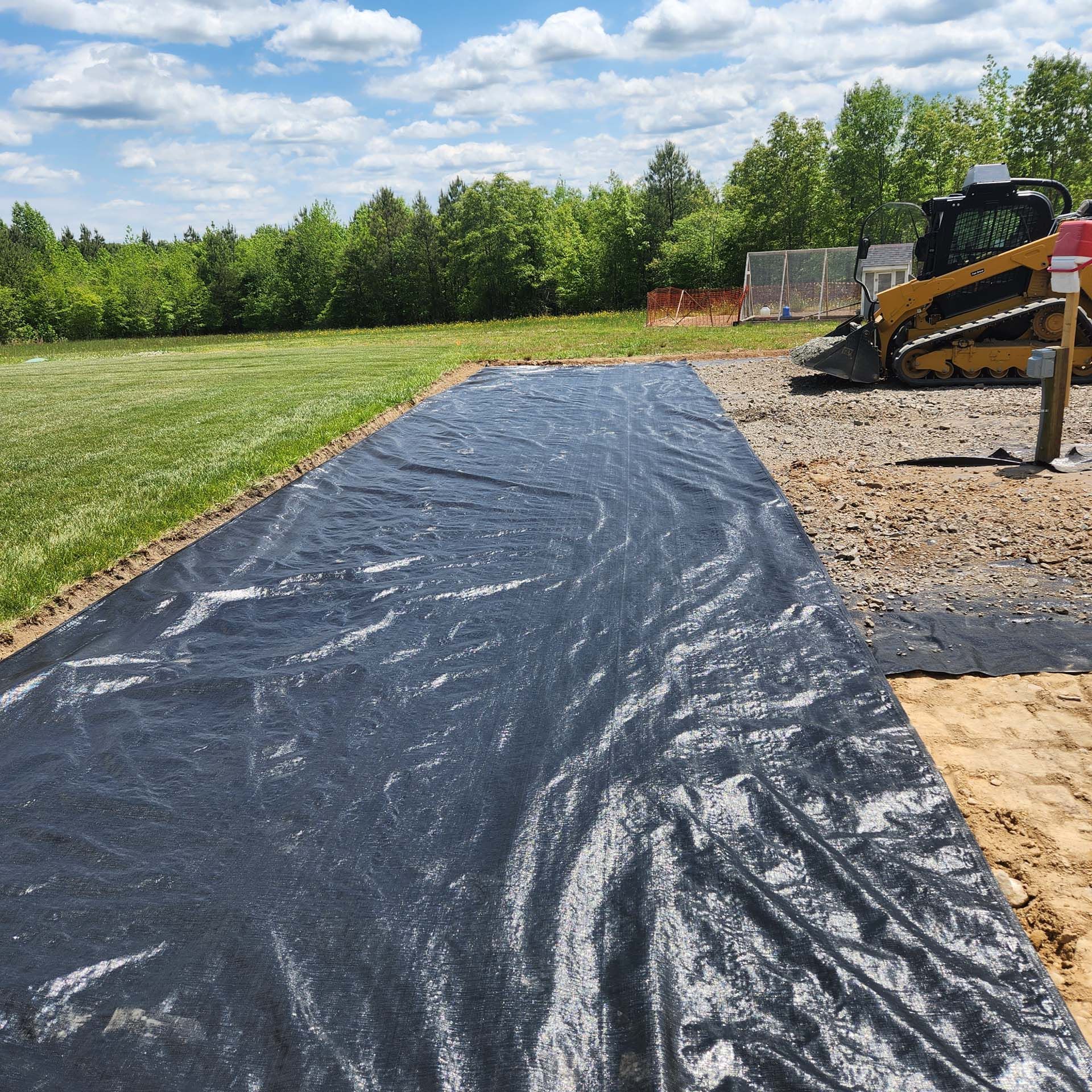 A black tarp is covering a dirt road with a bulldozer in the background.