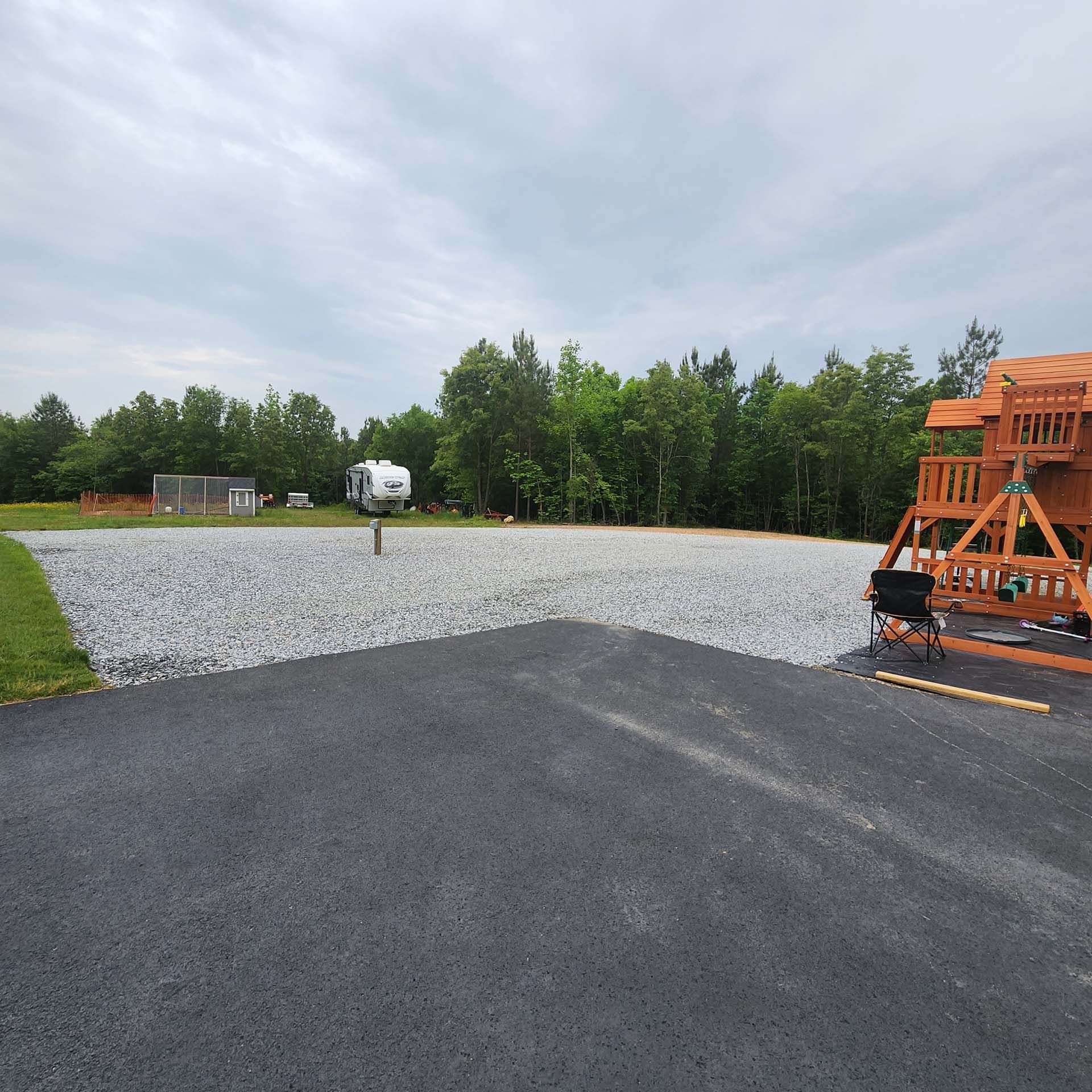 A wooden swing set is sitting on the side of a gravel road.