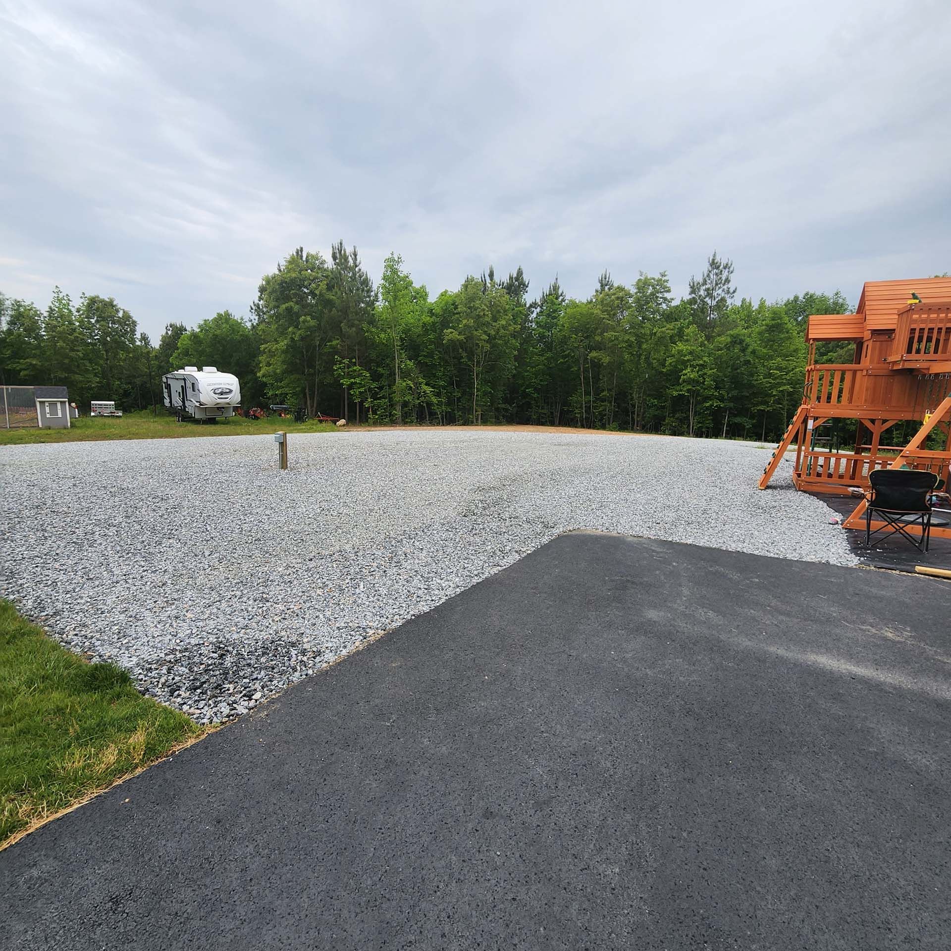 A rv is parked in a gravel lot next to a wooden swing set.