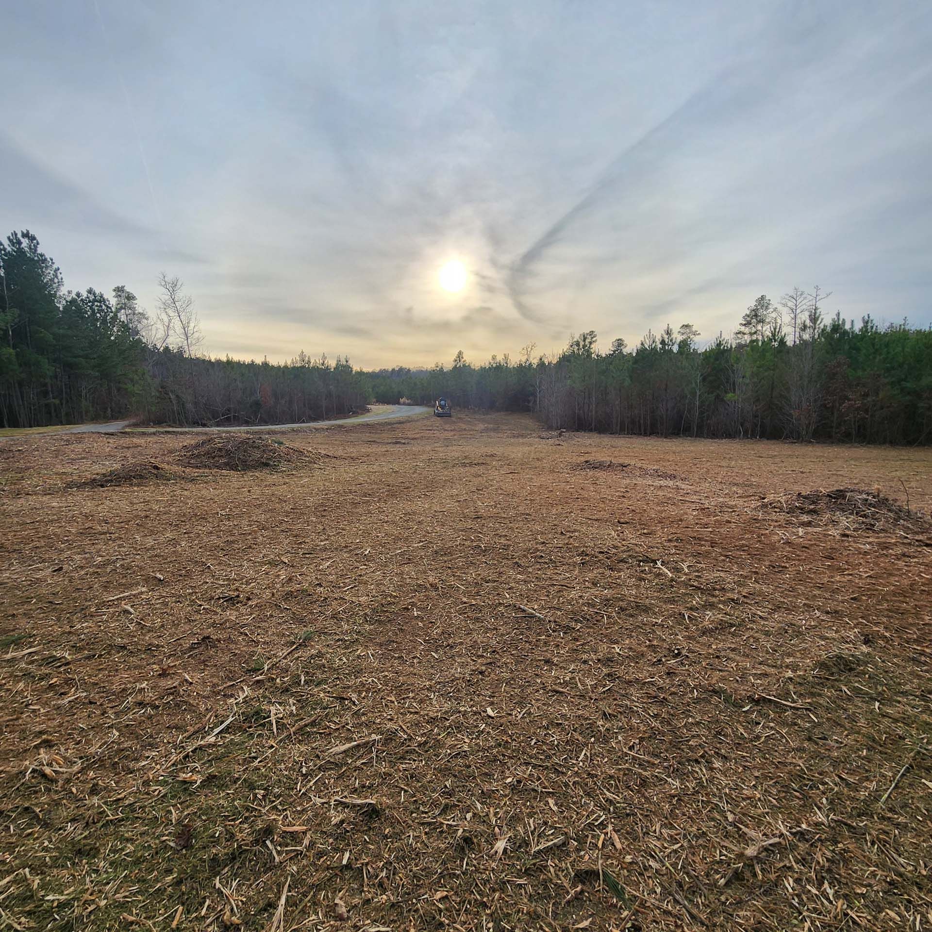 The sun is shining through the clouds over a field with trees in the background.