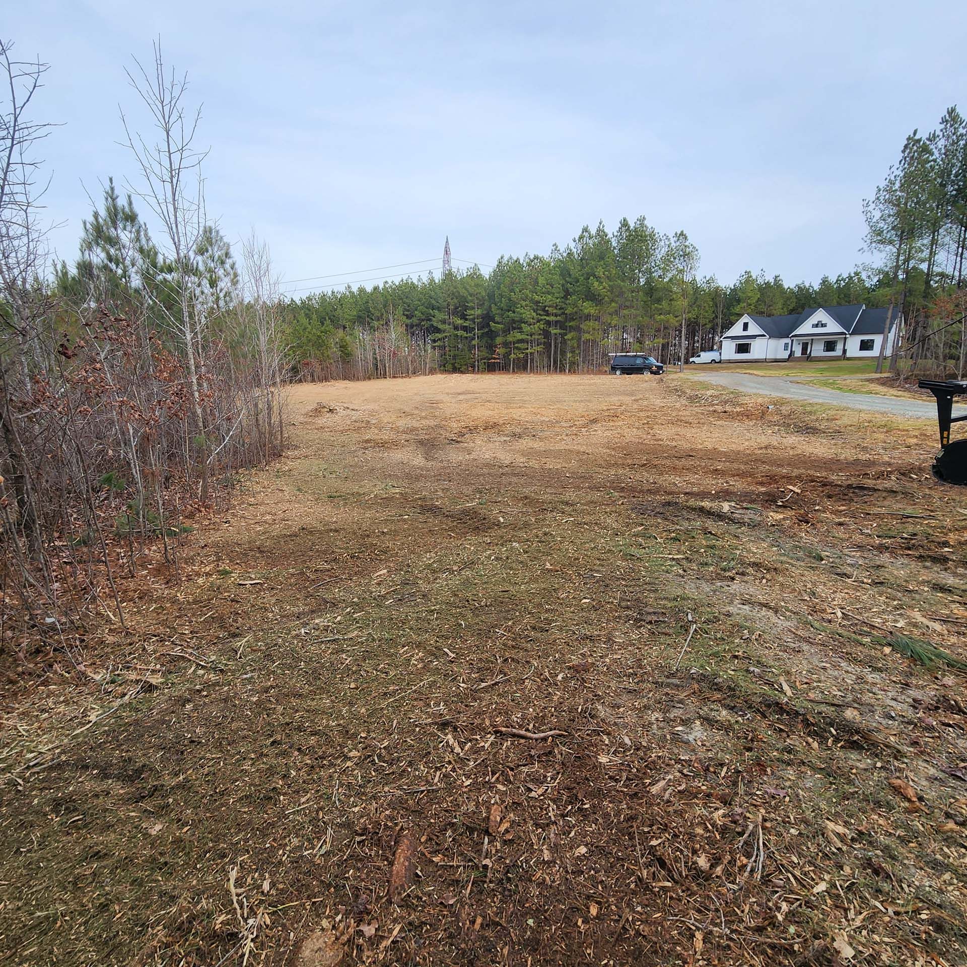 A dirt road going through a field with a house in the background.