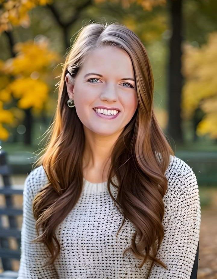 a woman in a sweater is sitting on a bench in a park and smiling .