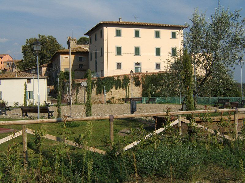 Un edificio beige chiaro con infissi verdi in un ambiente esterno soleggiato con una recinzione in primo piano.