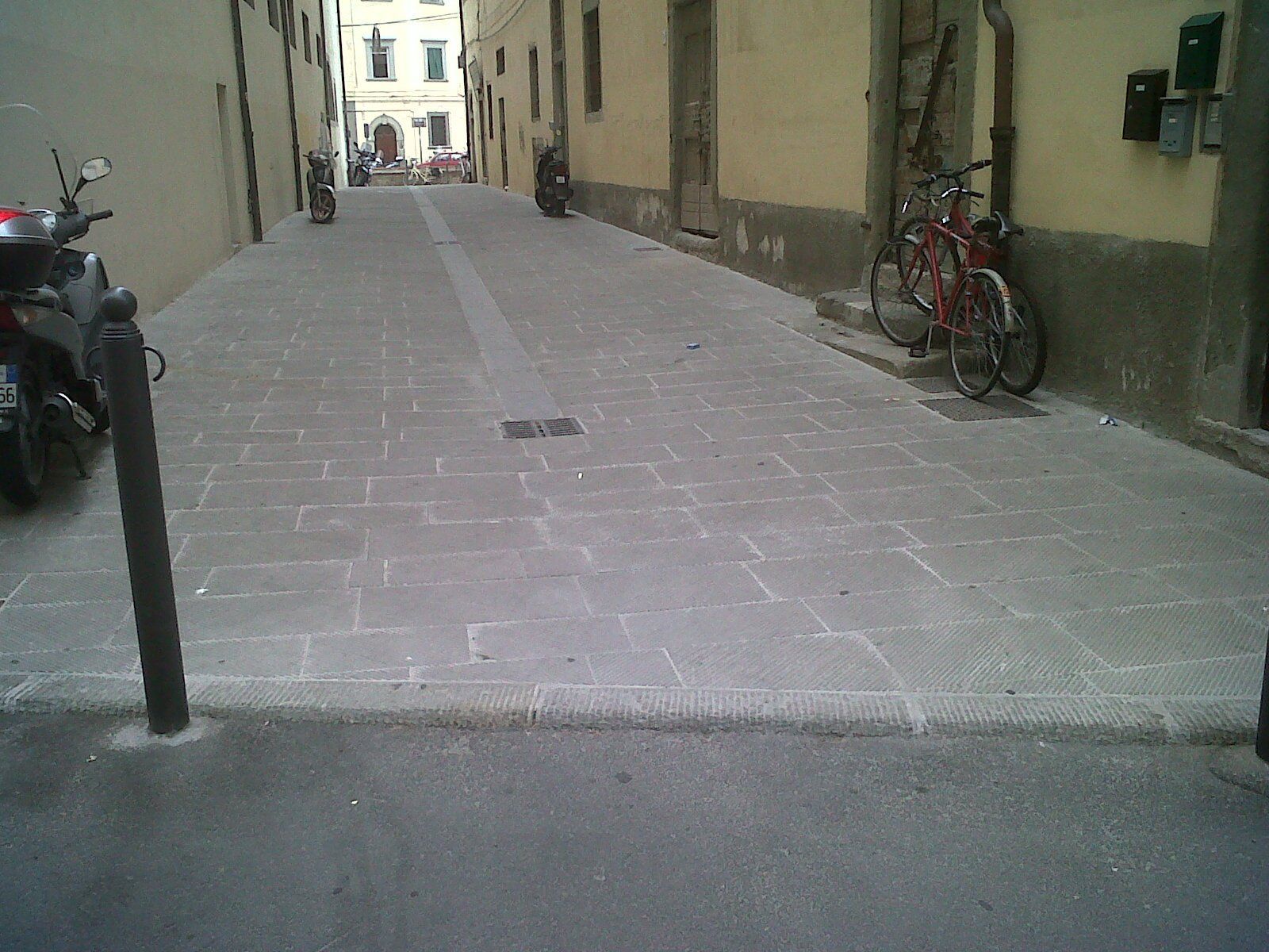 Stretta strada acciottolata fiancheggiata da edifici e biciclette parcheggiate. Motocicletta sulla sinistra.
