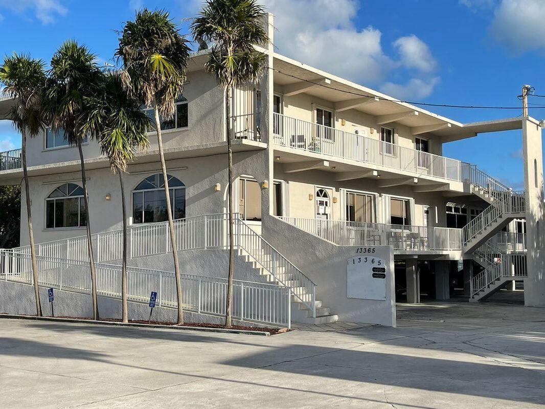 A large white building with stairs and palm trees in front of it.