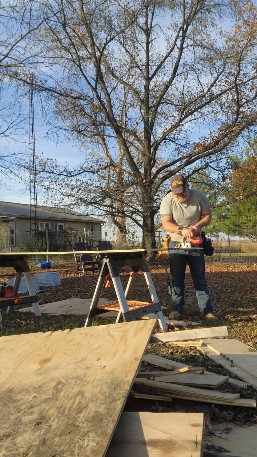 Person using a circular saw outdoors, cutting plywood on sawhorses. Sunny day.