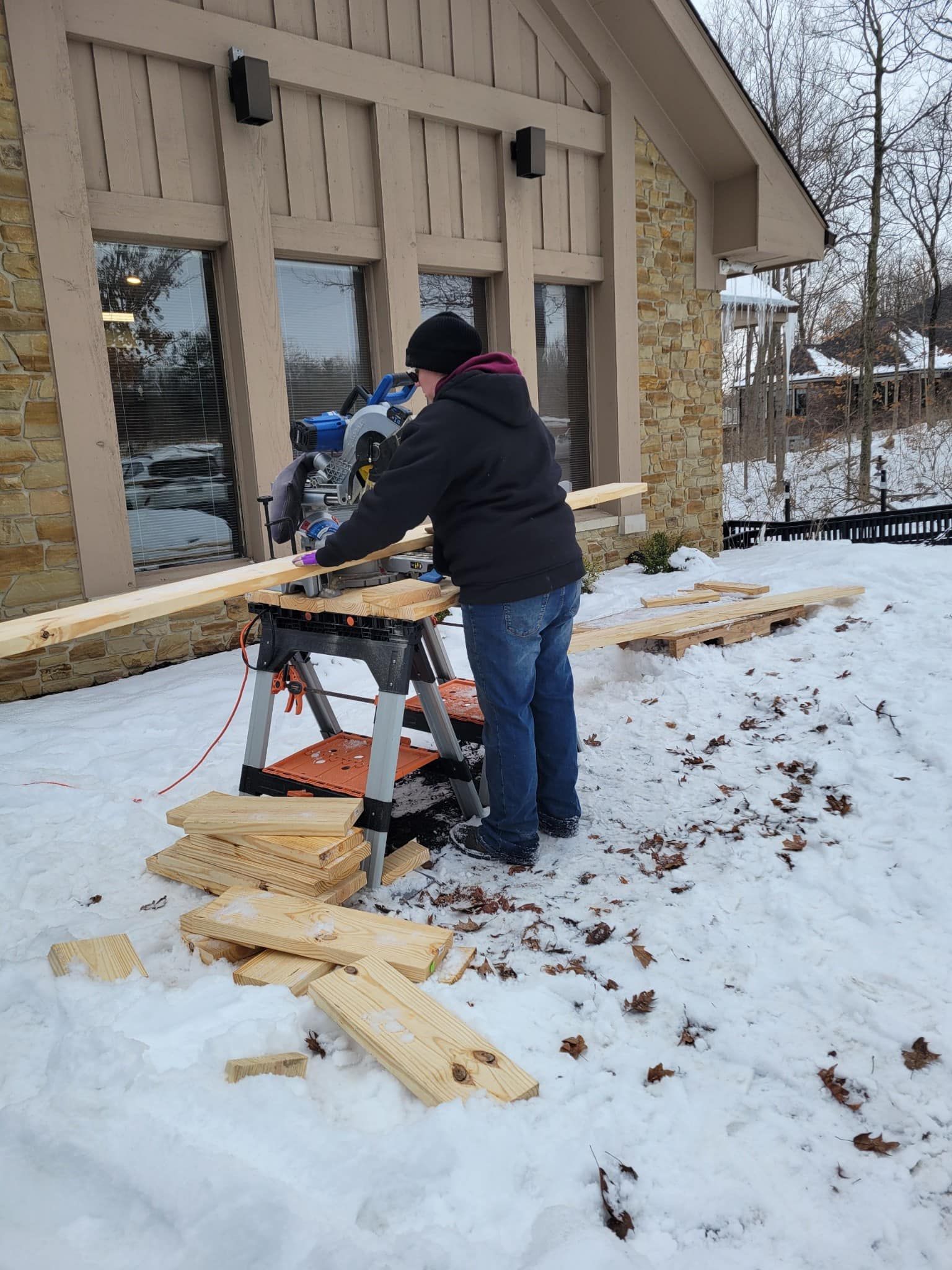 Person using a saw to cut wood outdoors in a snowy environment.