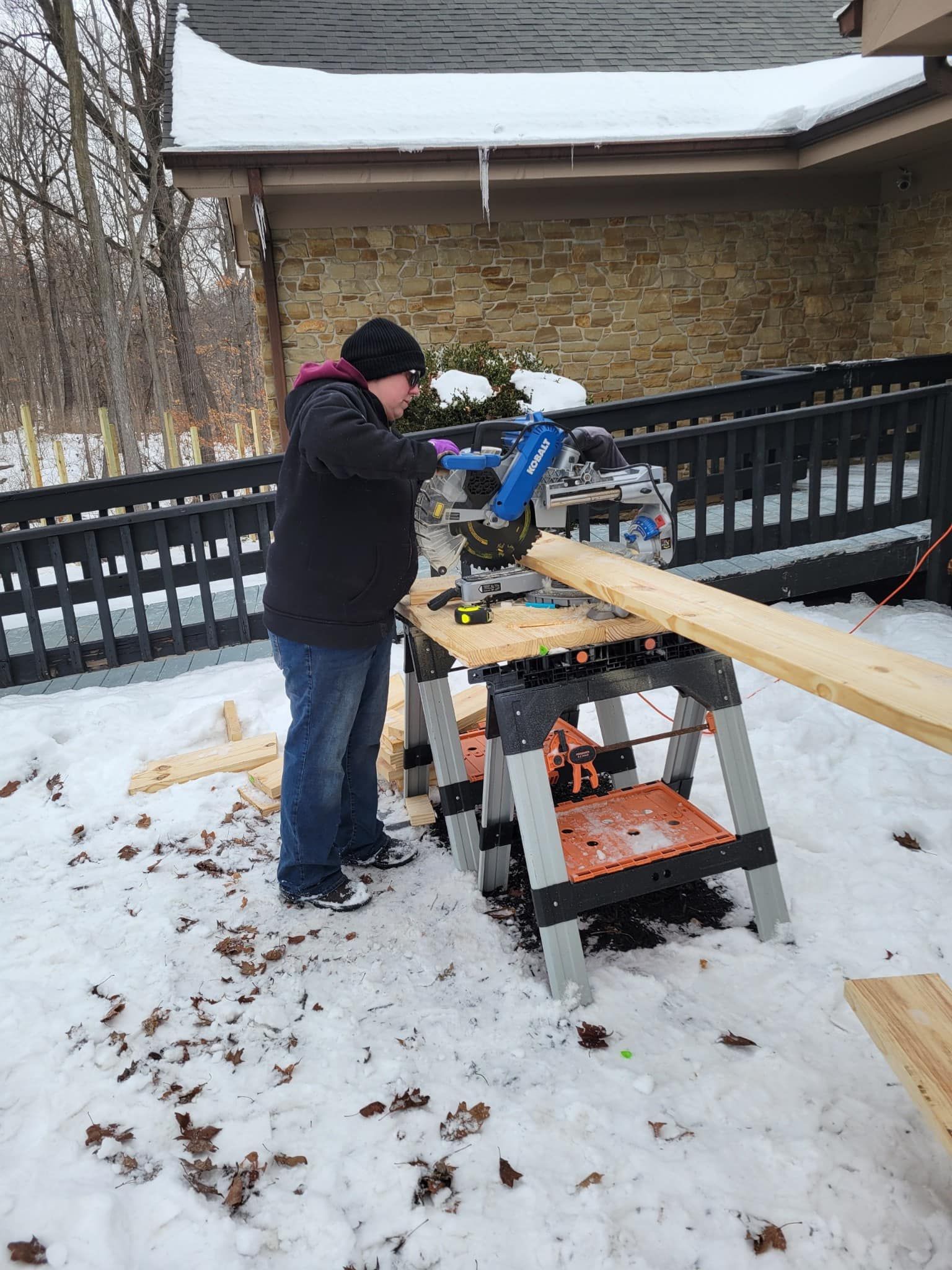 Person using a miter saw to cut lumber on a snowy deck.