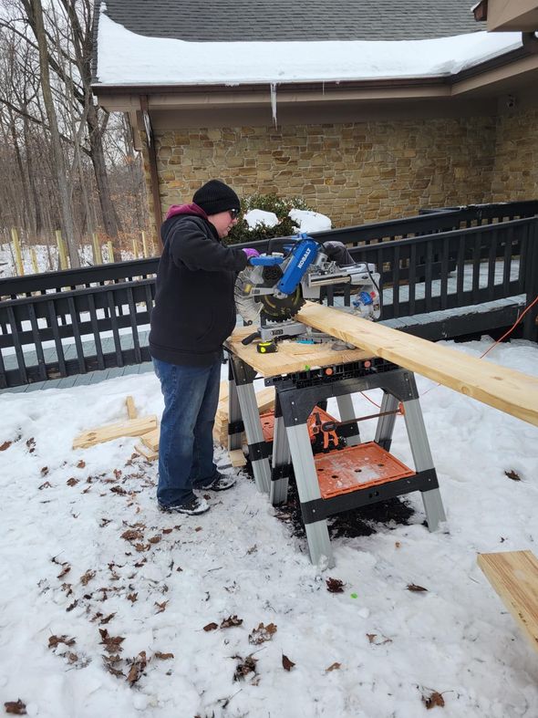 Person using a miter saw to cut lumber on a snowy deck.