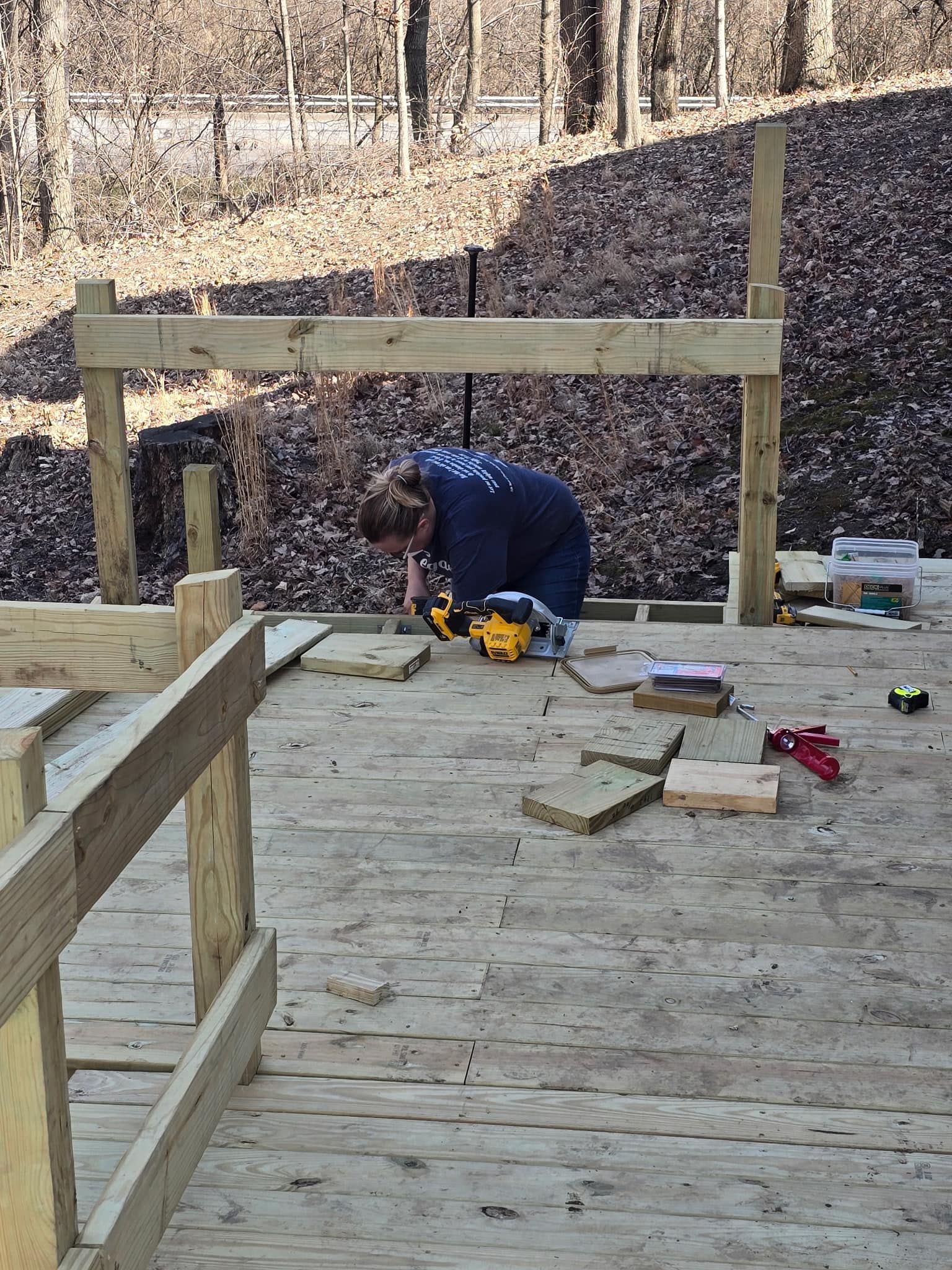 Person using a power tool to work on a wooden deck outdoors.