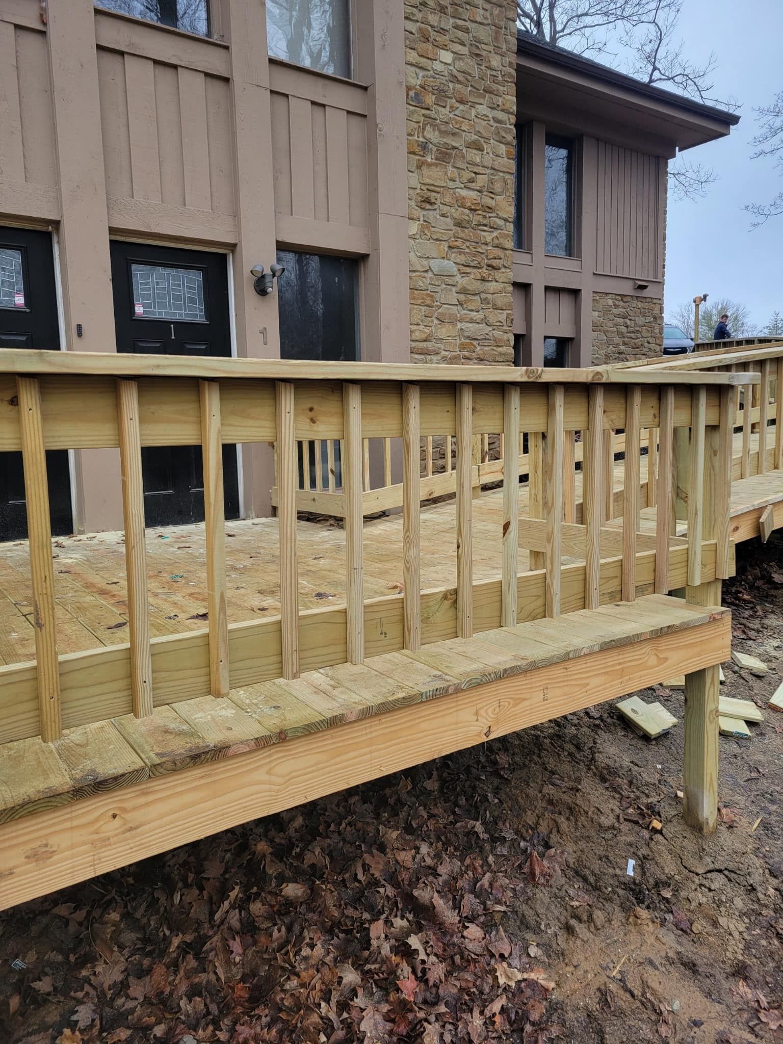 Wooden deck with ramp leading to a brown building with a stone chimney.