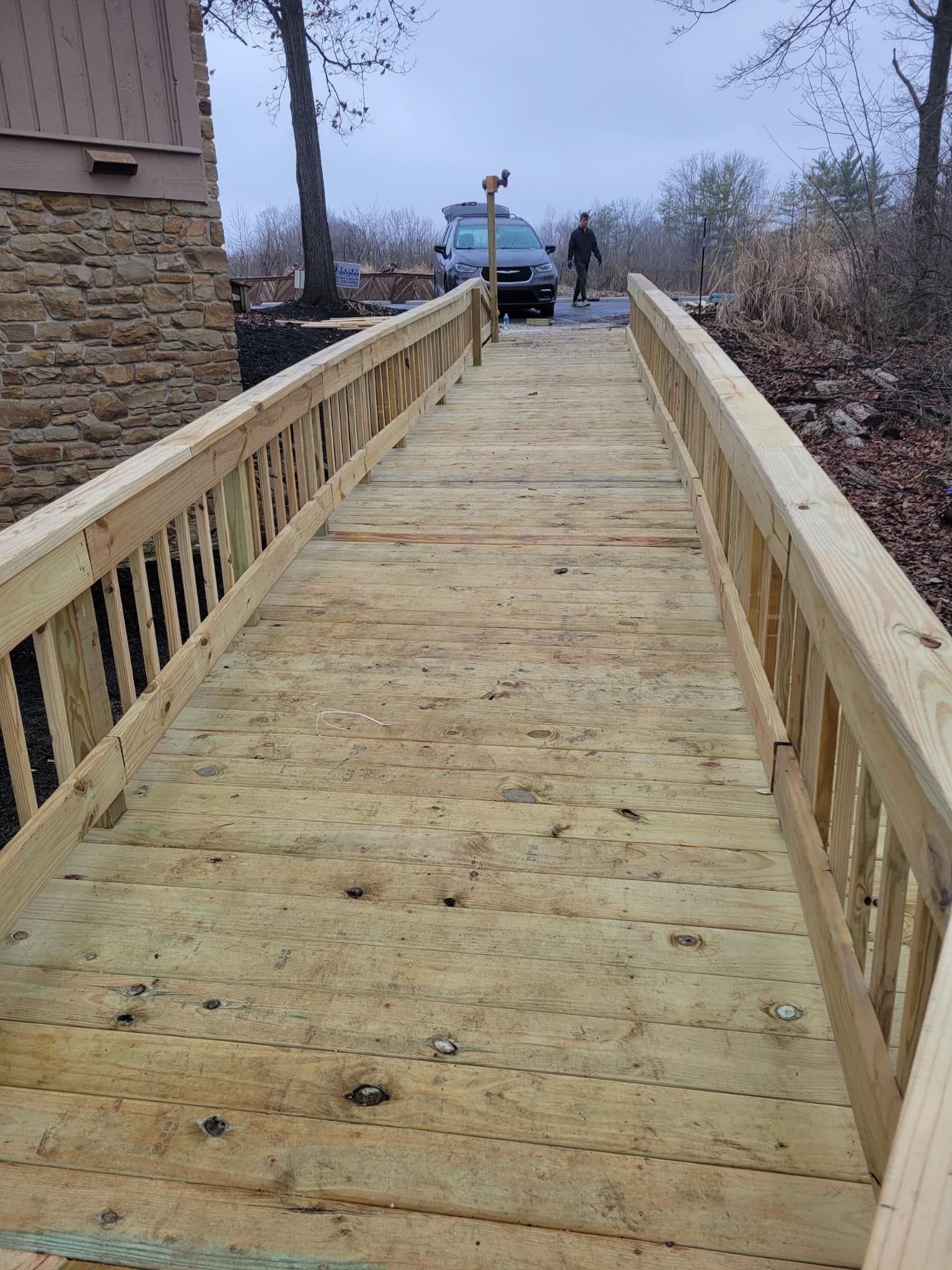 Wooden bridge with railings leading to a parked vehicle; person in the distance.