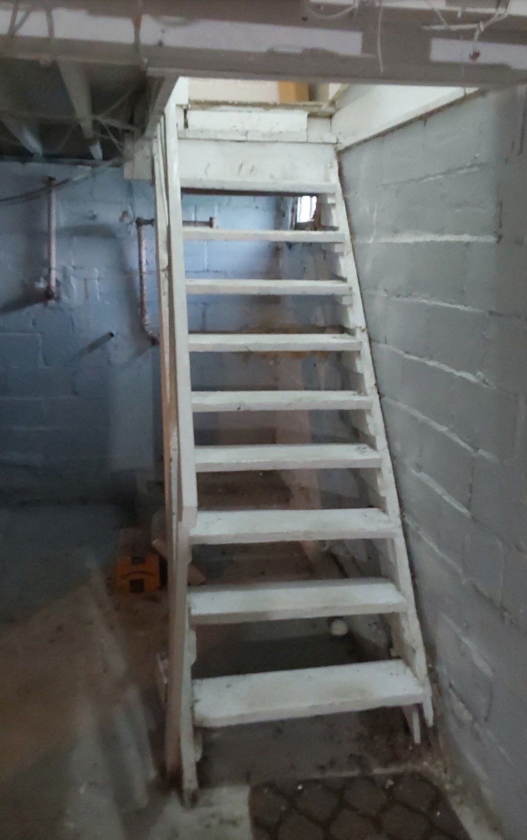 Wooden staircase leading up from a basement, white paint, concrete walls.