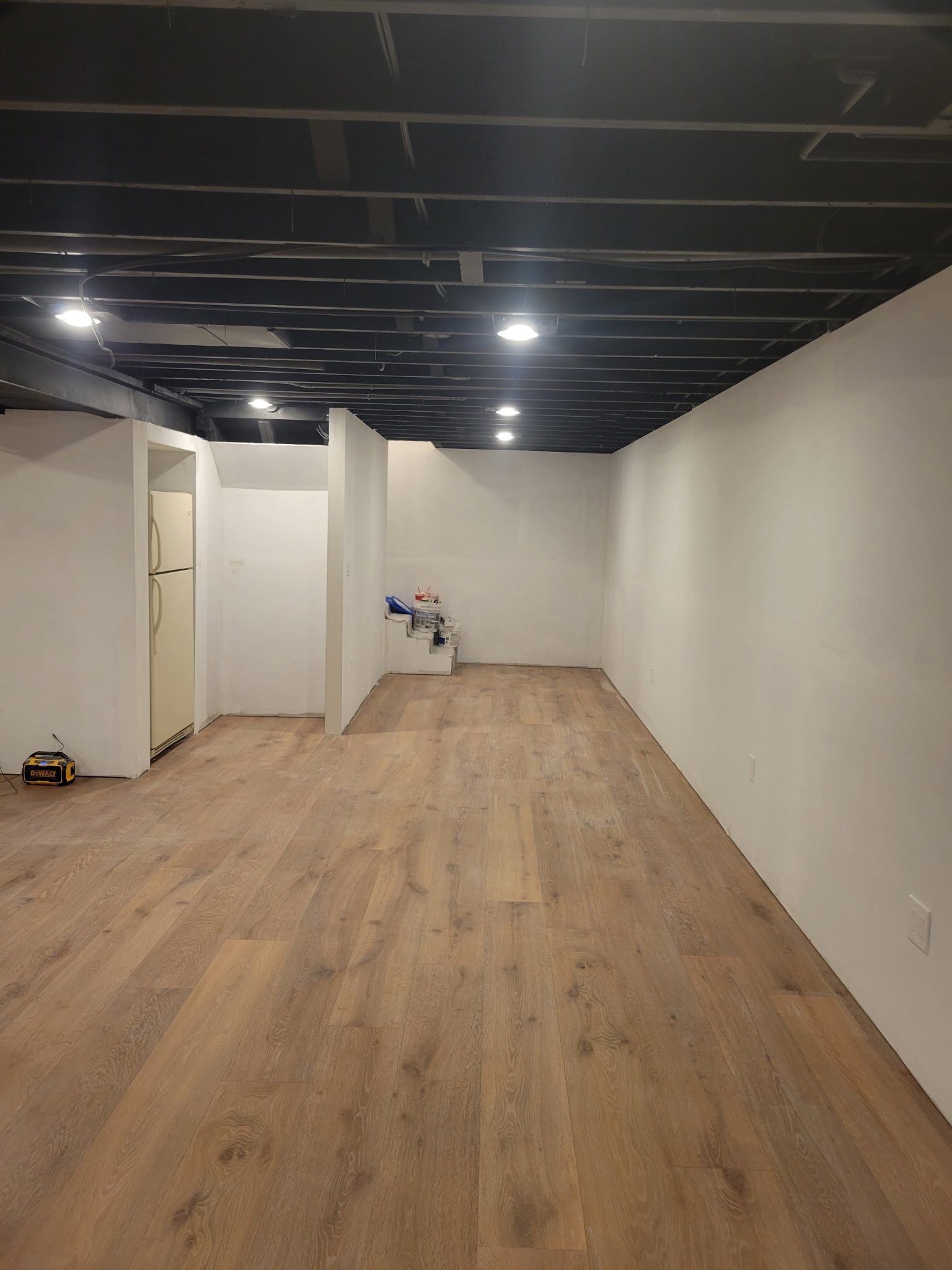 Interior view of a renovated basement with wood flooring, white walls, and a black ceiling with recessed lights.