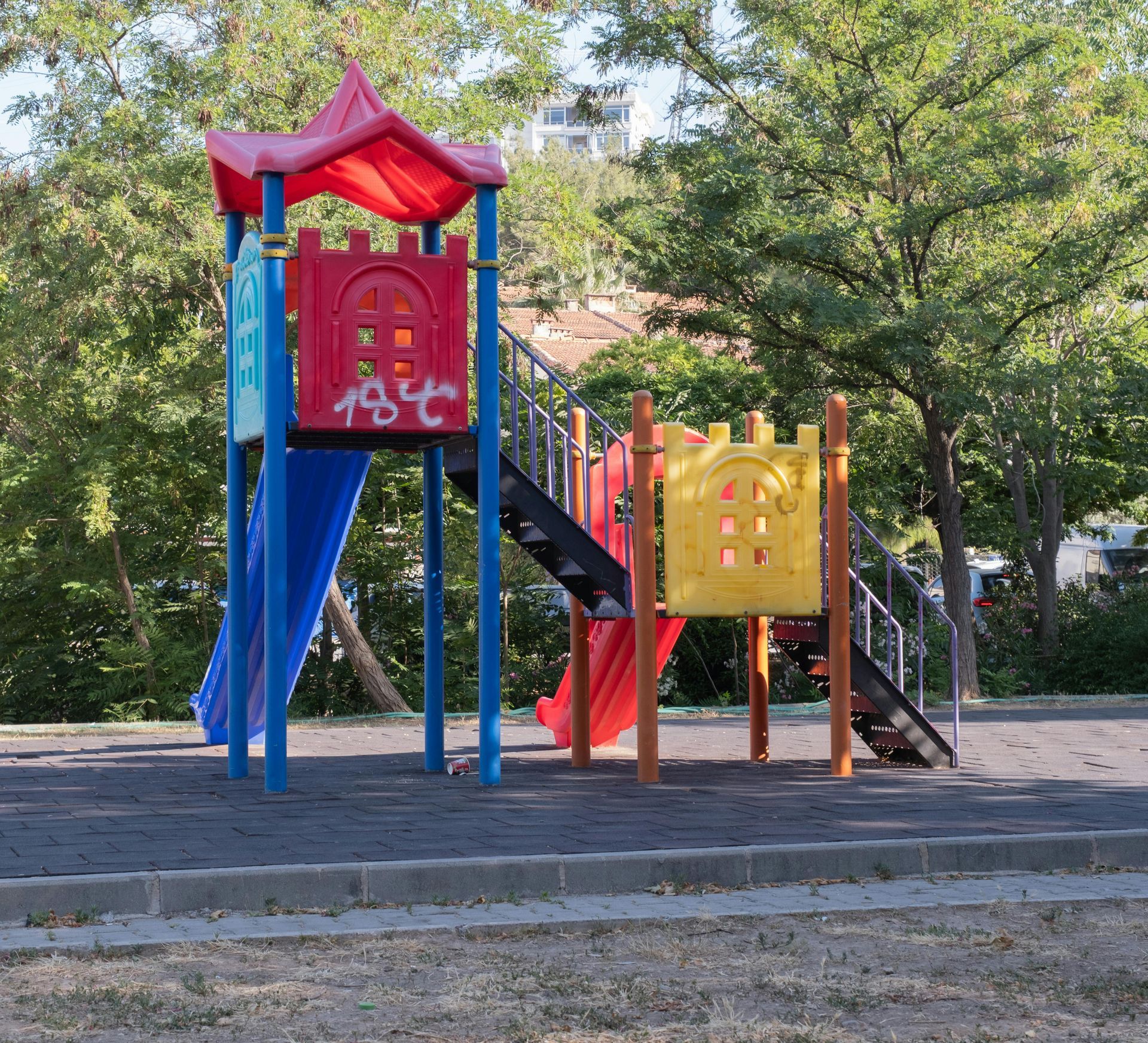Playground with blue, red, and yellow slides and climbing stairs, set in a park.