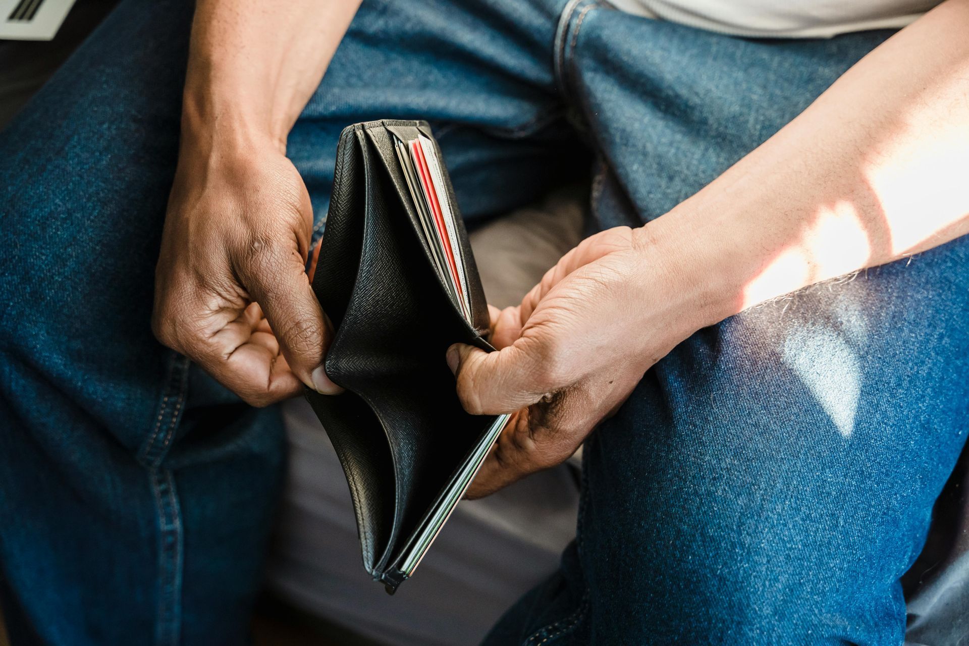 Person holding an empty black wallet open in lap, wearing blue jeans.