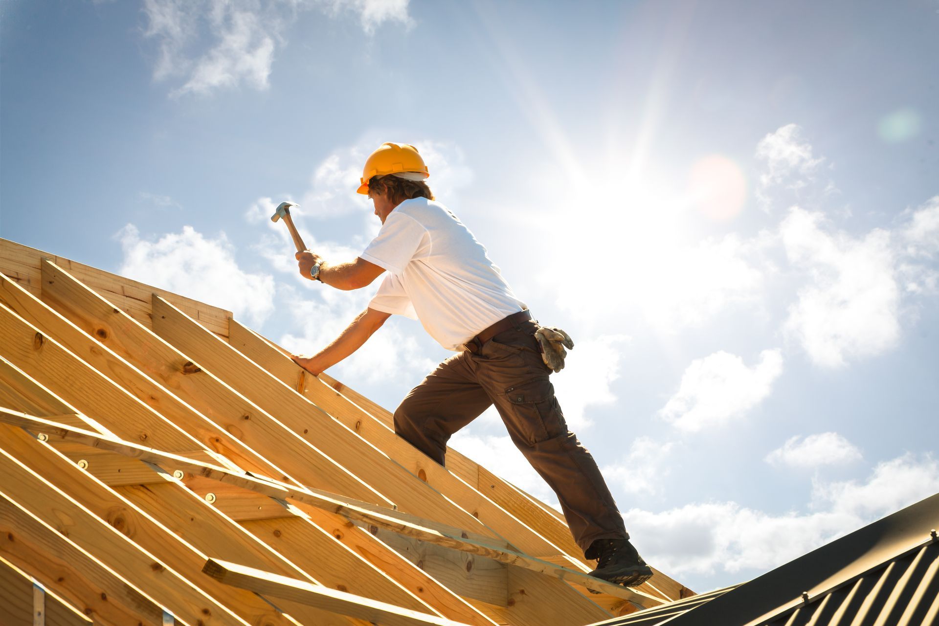 Roofing contractor installing wooden roof frame under bright sunlight during construction.