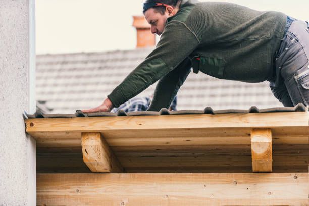 Worker installing corrugated roofing sheets on wooden structure for home roof repair.