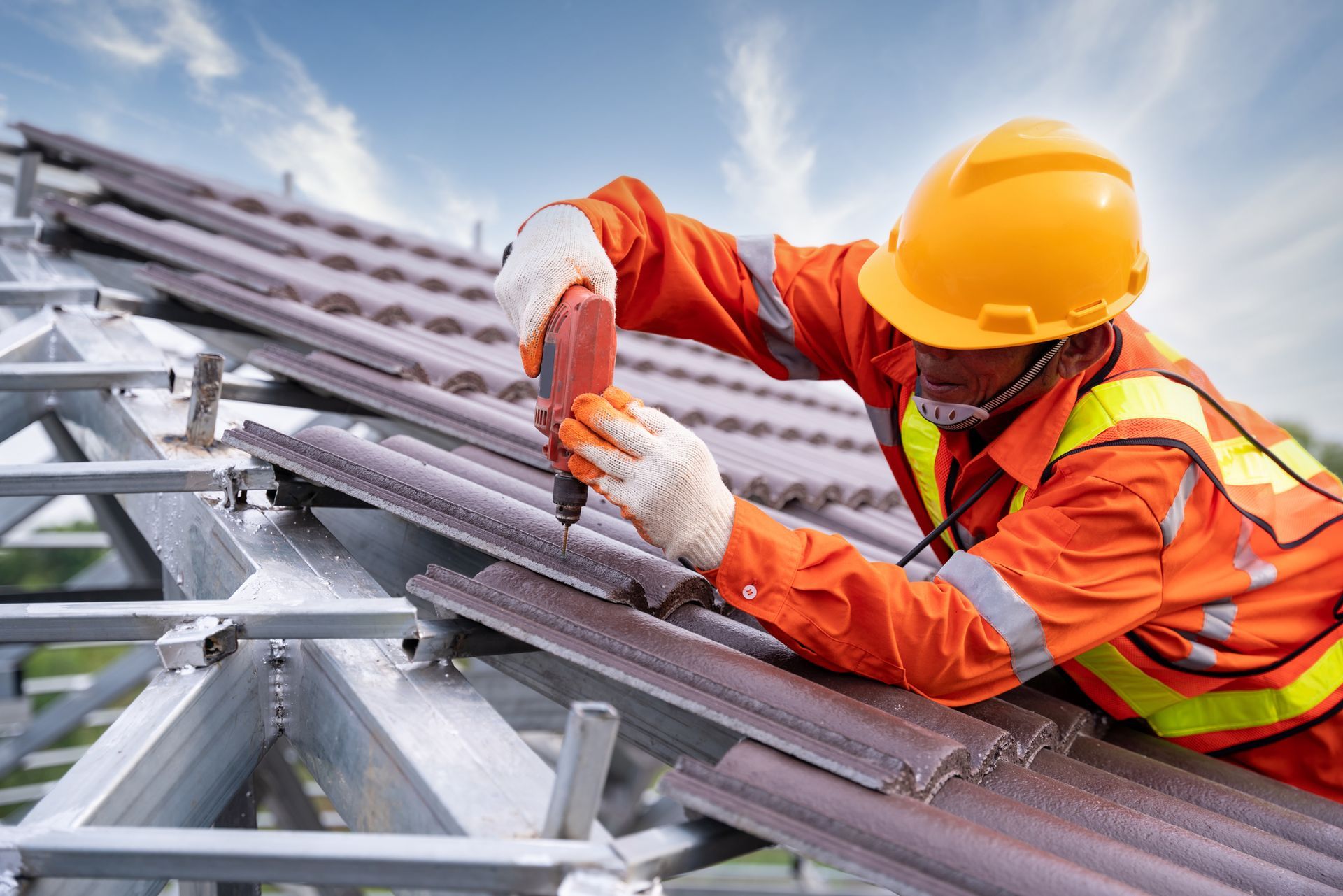 A residential roofing contractor, equipped with safety gear, is working on installing a roof.