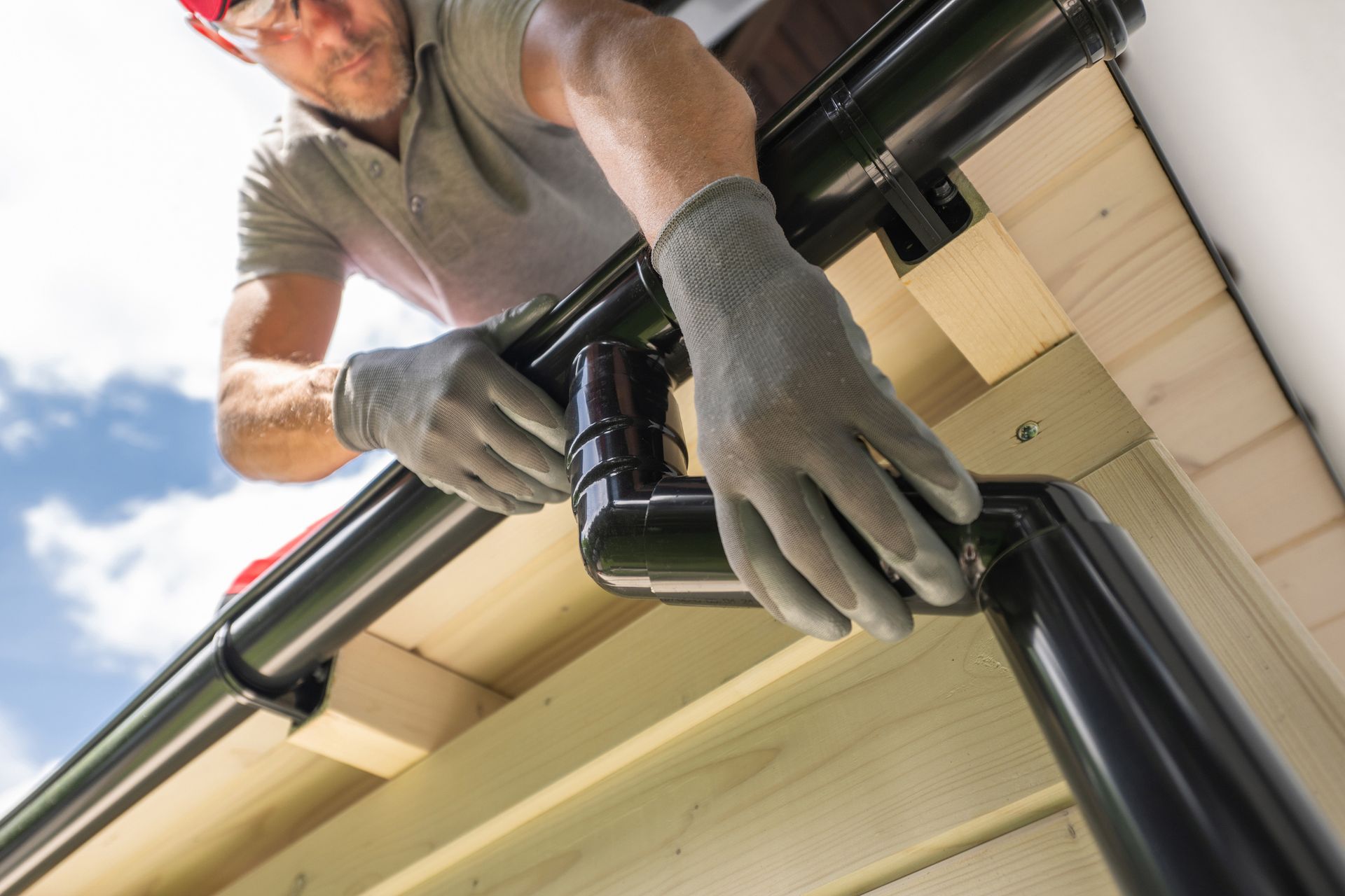 Roofing system contractor wearing gloves and safety glasses installing a black gutter.