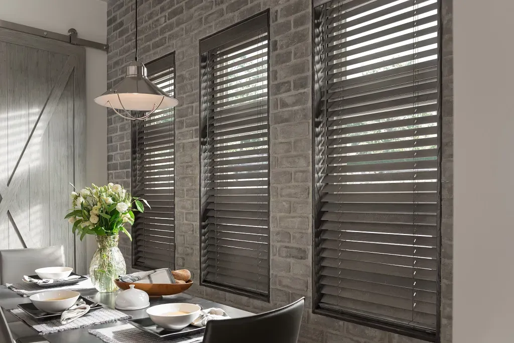 Dining room with dark gray horizontal blinds and brick wall, table set for meal.