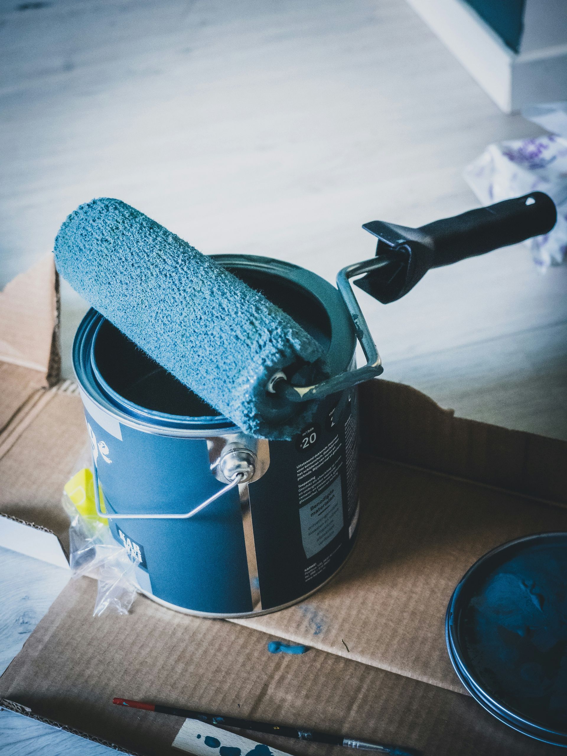 Paint can, open, with blue paint roller inside, on cardboard.