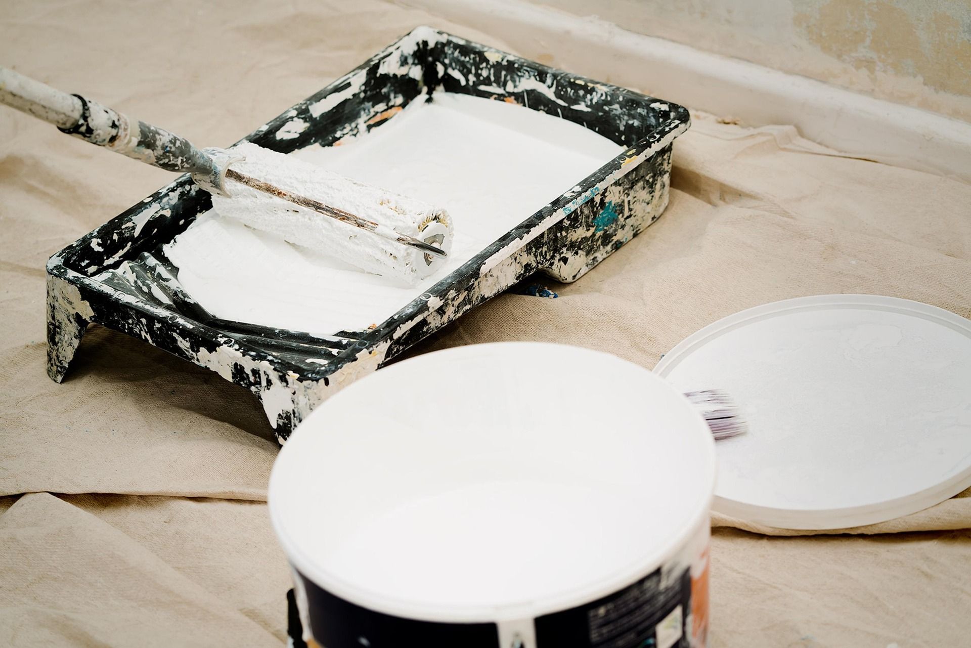 Paint roller resting in a tray filled with white paint, ready for use.