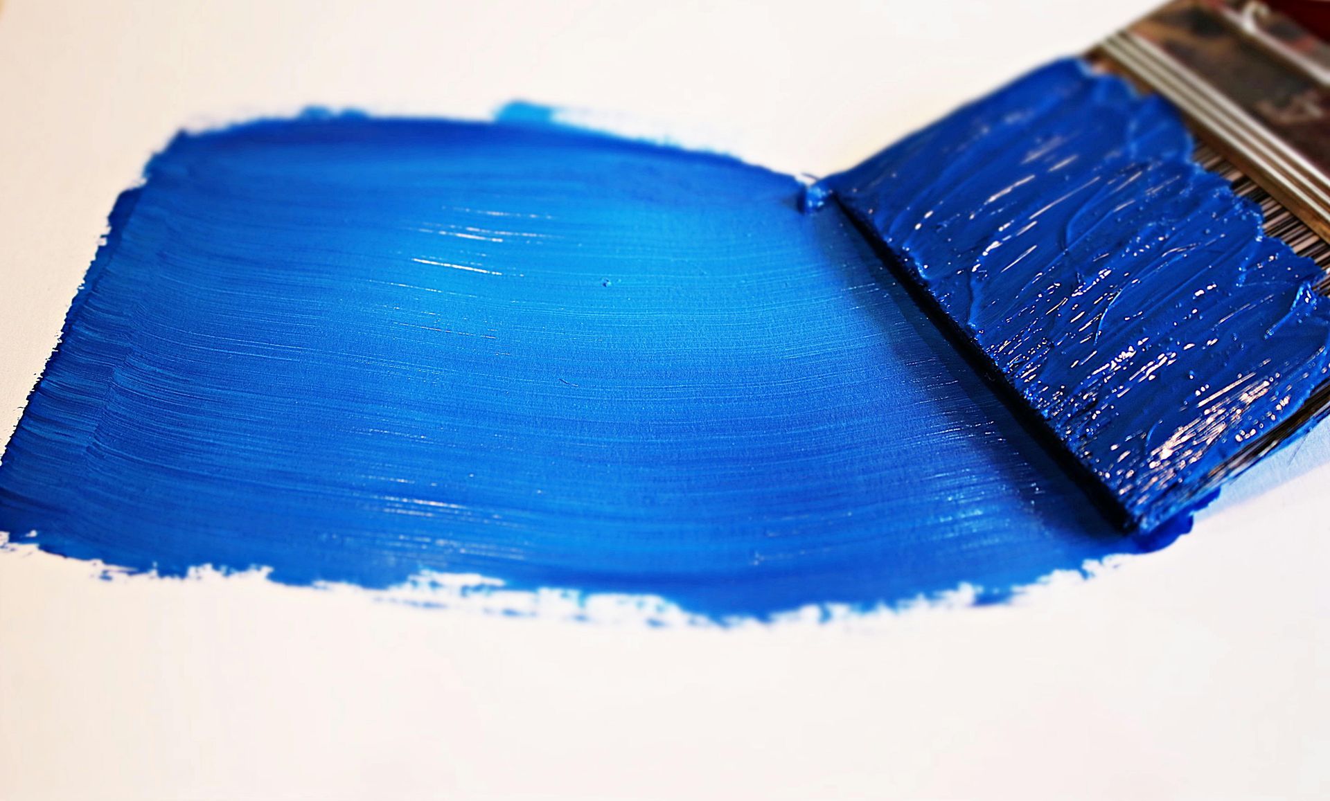 Blue paint being applied to a white surface with a paintbrush.