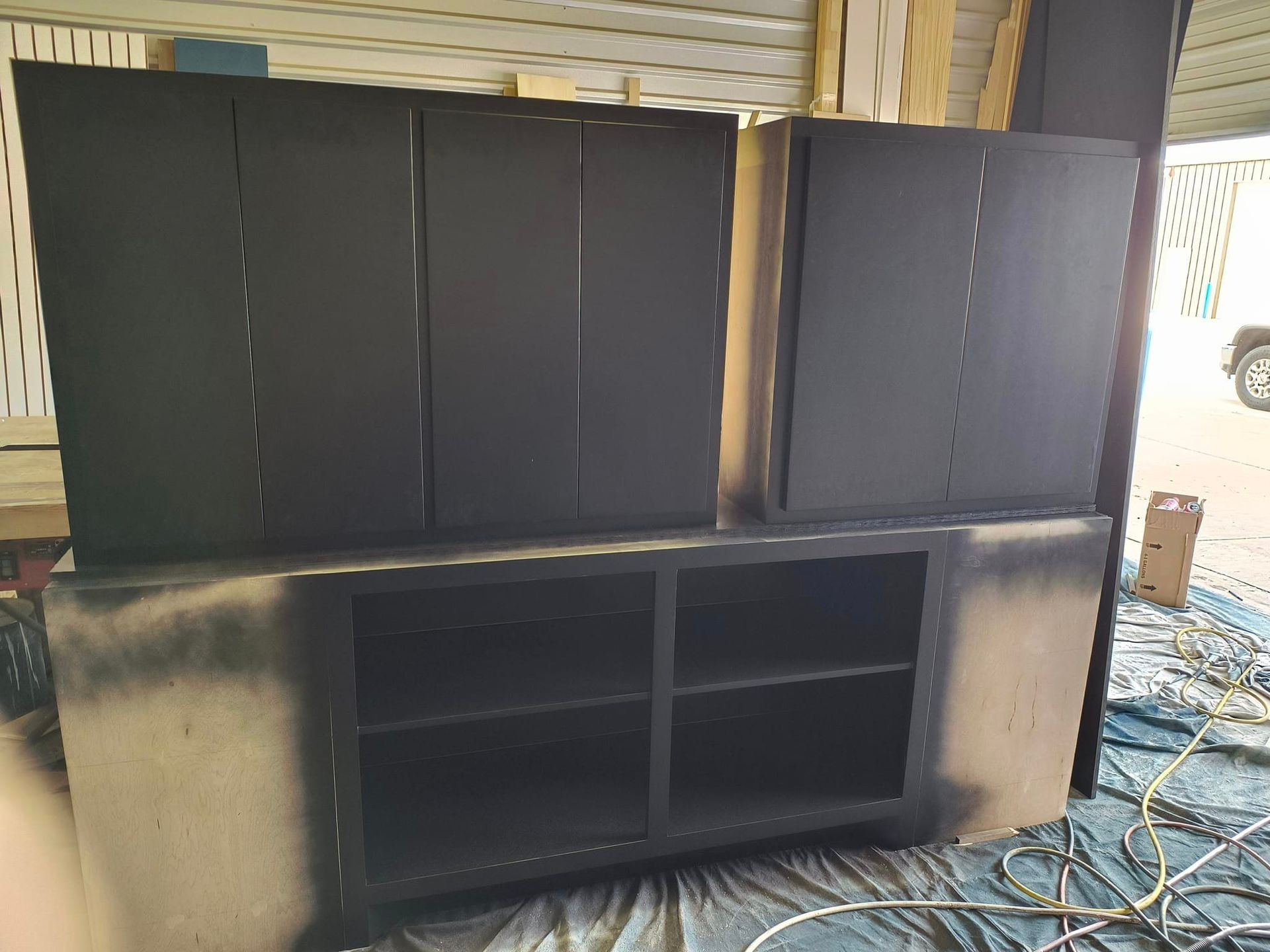 A black cabinet is sitting on top of a blue tarp in a garage.