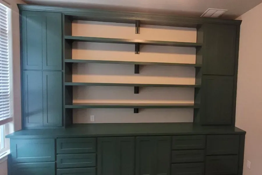 A room with green cabinets and shelves and a window.