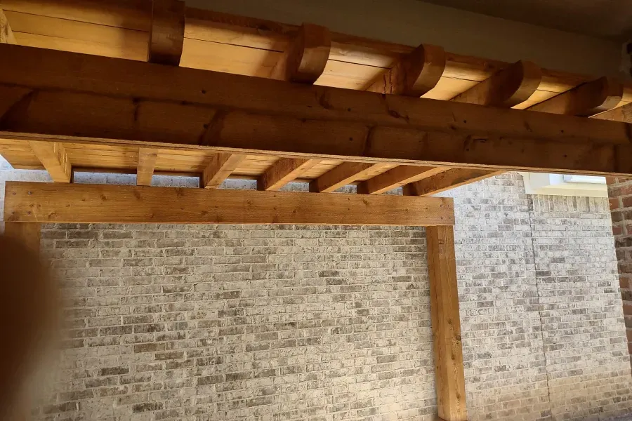 A wooden pergola is sitting on top of a brick wall.