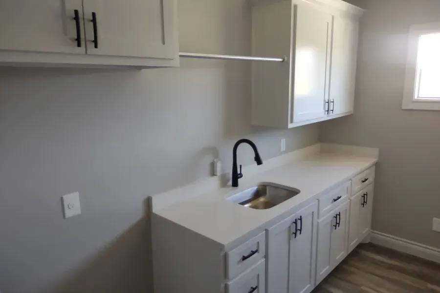 A kitchen with white cabinets , a sink , and a window.