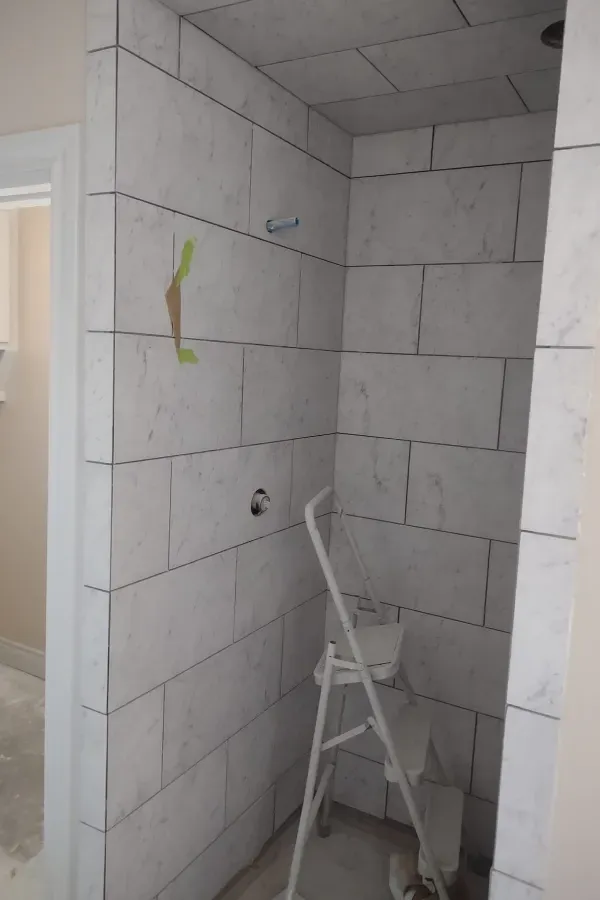A bathroom with white tiles and a ladder in the corner.