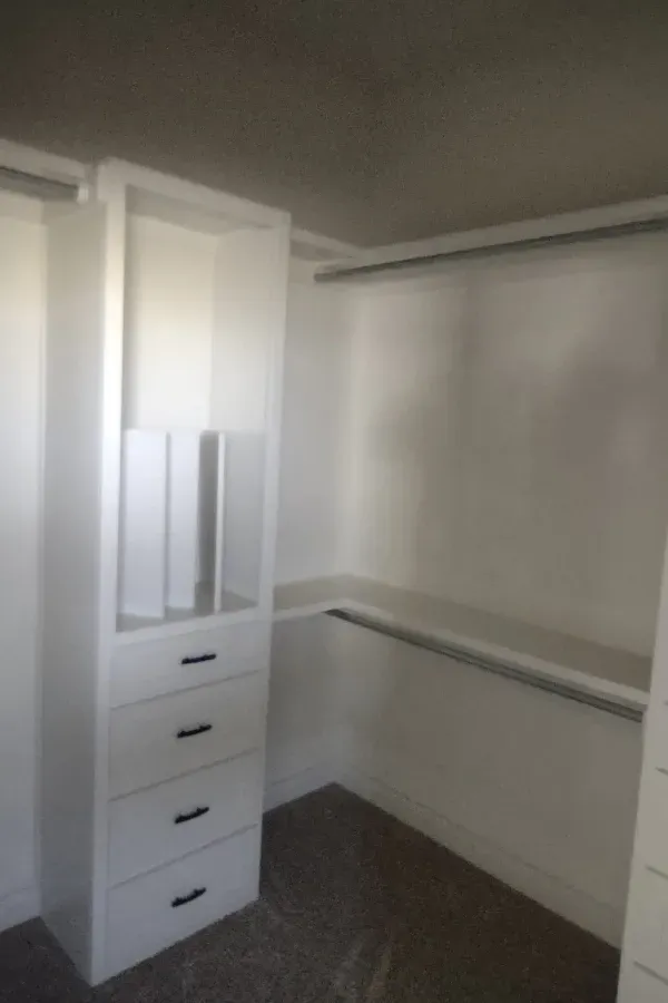 A walk in closet with white drawers and a mirror.